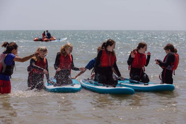 A group of young people wearing red life vests sit on paddleboards in the sea at Eastbourne