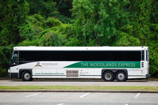 The Woodlands Express (aka Rodeo Shuttle) is a white city bus branded with "The Woodlands Township" and " THE WOODLANDS EXPRESS" along the side.