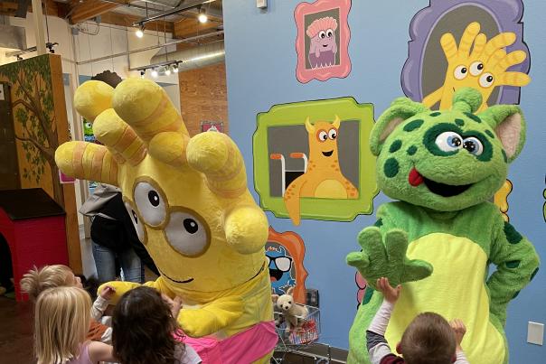 Three children playing with costumed mascots at the Children's Museum