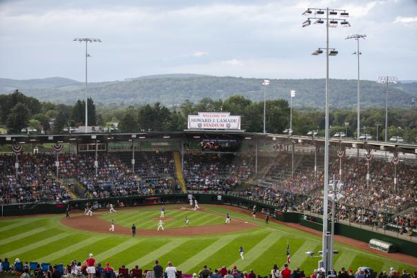 A baseball stadium filled with people watching a baseball game. A sign on the top of the stadium reads Welcome to Howard J. Lamade Stadium