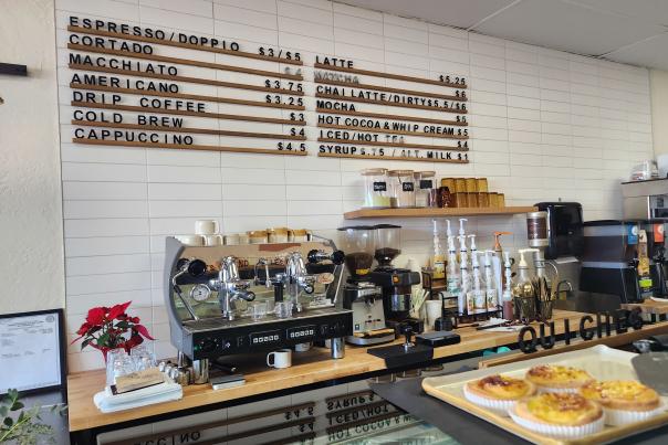 pastry lined coffee counter at Quiches & Pies with a listing of made to order coffees on the tiled wall