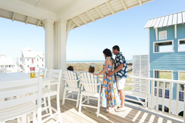 Couple standing on a white beach house porch overlooking the ocean at Cinnamon Shore.