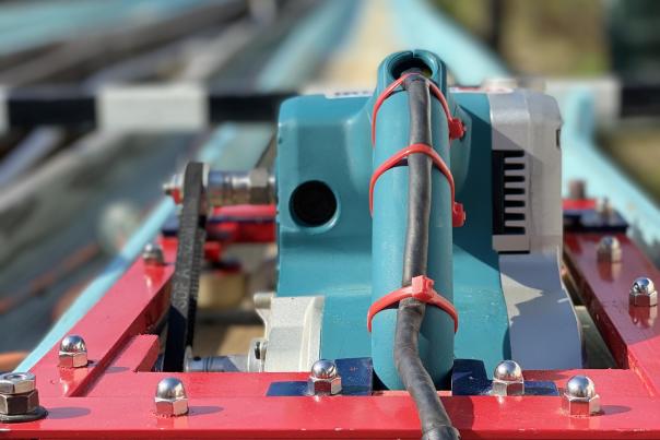 A teal and red belt sander is in focus on a wooden race track