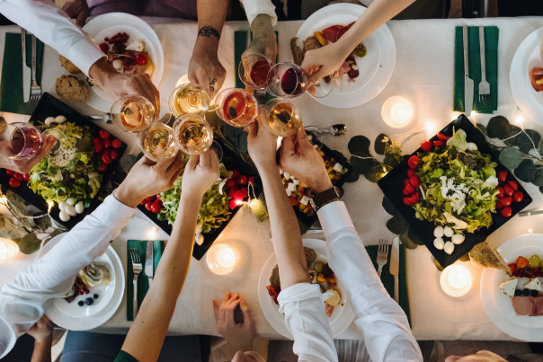 Group of friends and family cheers their wine glasses over a dinner table with a white table cloth and appetizers.