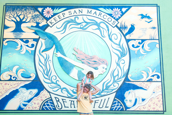 Father and daughter pose in front of a mural of a mermaid.