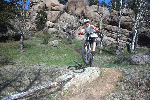 A mountain biker rides over a rocky section of singletrack trail at Curt Gowdy State Park in southeastern Wyoming. Large granite rock formations, trees, and open terrain surround the trail, highlighting the park’s technical mountain biking and outdoor recreation opportunities.