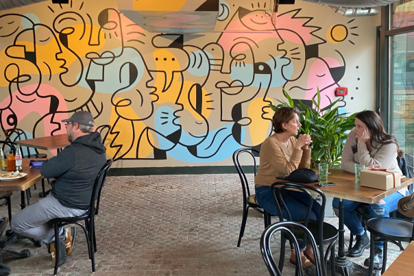 A table with two white women sit at a table at Bandit Tacos in front of a colorful mural of abstractly drawn faces