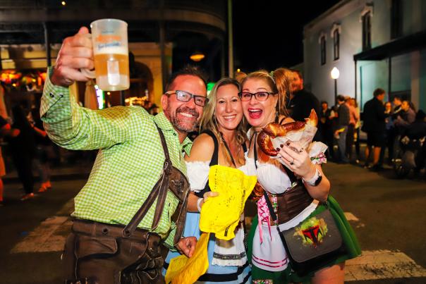 Two women and a man holding a beer bug and a pretzel