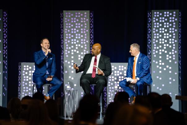 Jevon Gibbs, Aaron Cox, and Brad Bailey speak at The Woodlands Chamber of Commerce's 2026 Economic Outlook Conference. The three men are on stage with light-up props resembling a city skyline.