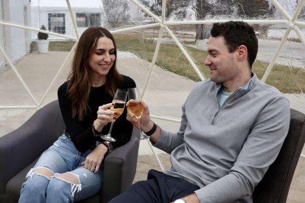 A man and woman clink together champagne glasses in an inflatable igloo at Aubrey Vineyards