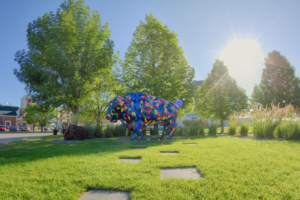 multi-colored painted bison statue in front of green trees in the sunshine