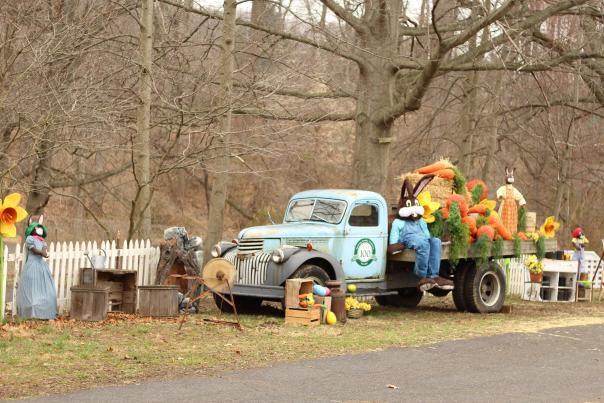 A vintage truck with an Easter bunny and large, fake carrots on the bed of the truck