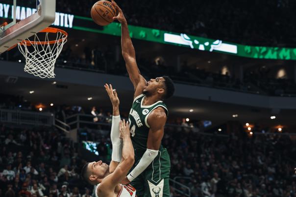 A Milwaukee Bucks player leaps toward the basket for a layup over a Chicago Bulls defender during a packed home game at Fiserv Forum.