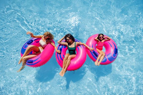 Two women and a girl each lounge in a raft on calm pool water