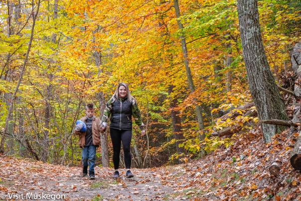 Mother and son walk holding hands along autumn colored trail in Muskegon State Park. The little boy holds a football.