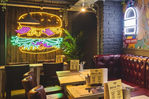 Beefy Boys interior with tables with red seat backs and large neon burgers on the wall