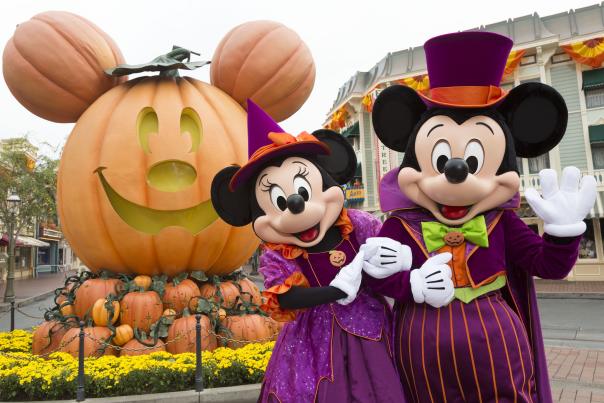 Image of Mickey and Minnie Mouse dressed up for halloween, standing in front of a Mickey-shaped giant pumpkin on Main Street U.S.A. inside Disneyland Park.