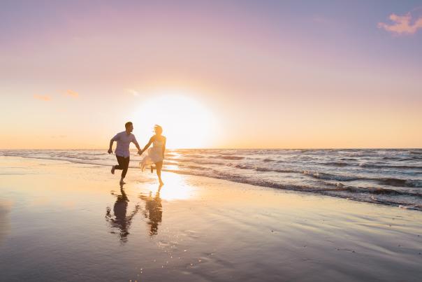 A couple runs hand in hand along the beach