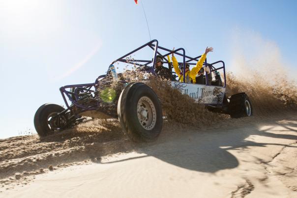 Passengers throw their hands up in the air as dune buggy descends a sand bank.