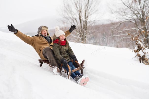 A grandfather and granddaughter take a sled ride in the snow.