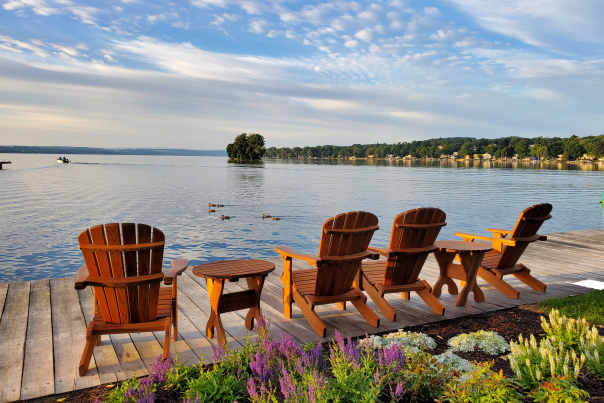 Adirondack chairs on a dock over looking Canandaigua Lake on a sunny day. Skenoh Island can be seen in the distance.