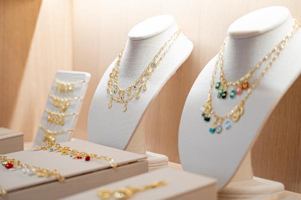 A display at gorjana features two neckline standees wearing gold chain-link necklaces with small, colorful charms. Three flat standees display matching bracelets and anklets.