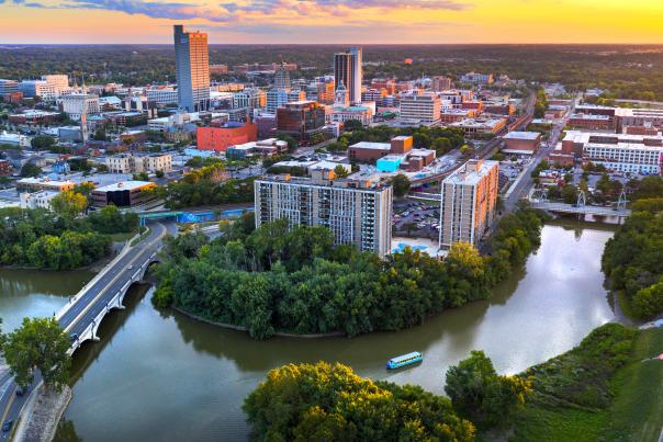 Drone shot of downtown Fort Wayne, Indiana at sunset with the confluence of the St Marys and St Joseph Rivers in the foreground and the skyline in the background. The Sweet Breeze canal boat is sailing on the St Marys River.