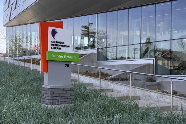 Modern exterior view of the Columbus Metropolitan Library – Dublin Branch, featuring glass walls and the vibrant green and orange library sign at 75 N. High Street.