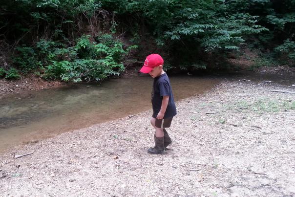 A young boy heads for the creek in his rain boots for some creek stompin' fun at Burkhart Creek Park near Martinsville, Indiana.