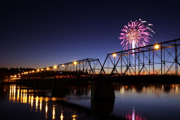 Fireworks bursting at night over a bridge on a river