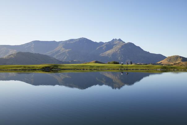 Wide shot of a golf course with lake reflecting mountains