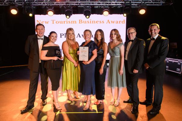 people stood on a stage in front of an awards screen in black-tie attire with an award in hand