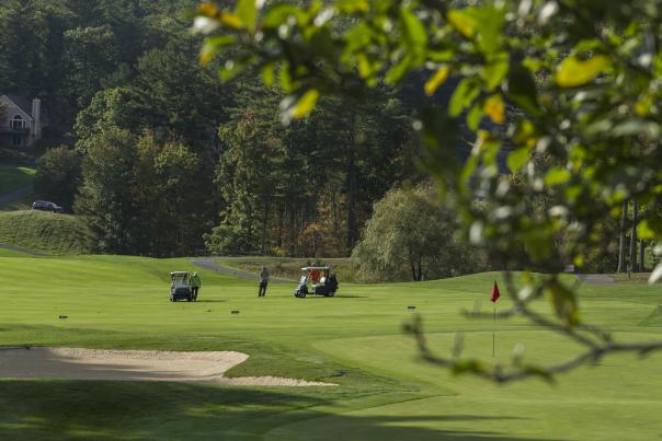 Two golf carts in the distance with a golfer setting up a shot