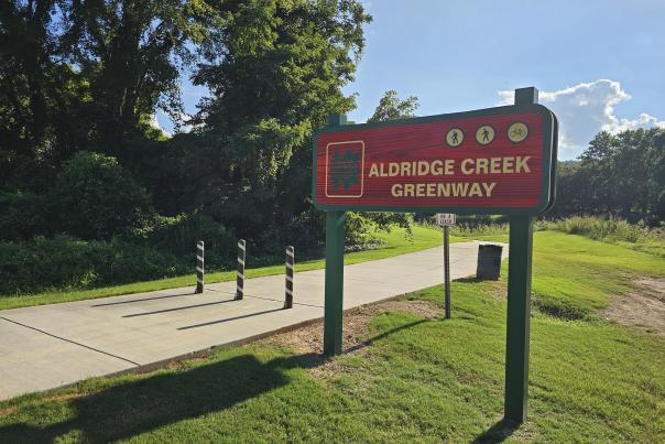 The Aldridge Creek Greenway sign next to a walking trail