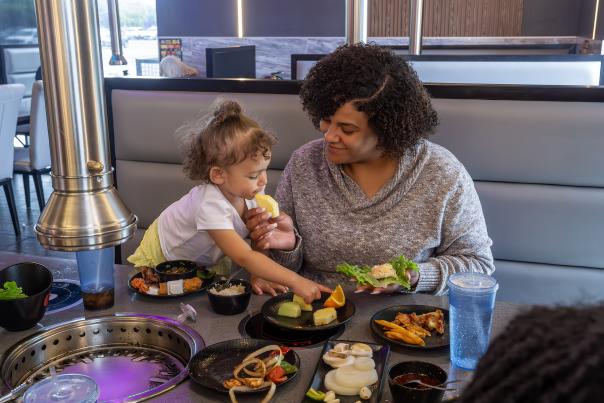 Mother and daughter enjoying a meal together at KPOT Korean BBQ & Hot Pot, cooking food at the table grill and smiling as they share dishes.