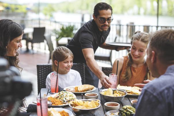 Located at Cantina Laredo in the Branson Landing. There is a family of 5, two parents and three daughters, enjoying a large meal on the patio of the restaurant. They are seen war various foods, drinks and even dessert.