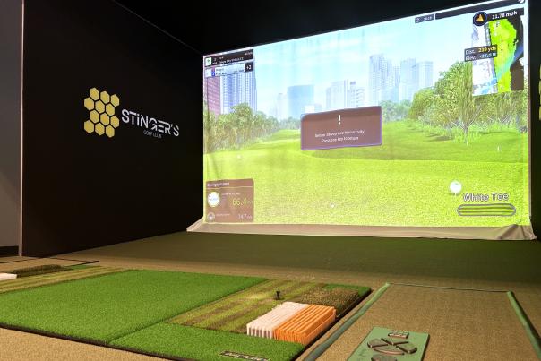 Indoor golf club bay with turf square and large screen displaying a course simulation.