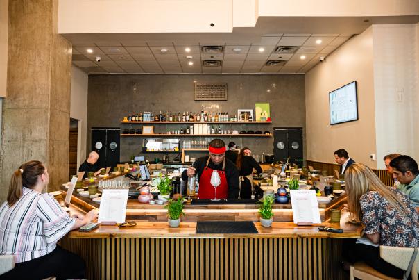 The Kokoro handroll bar forms a "u" around the dining room. Six guests are seated at the bar, a chef in red prepares a drink near the viewer, and rubber ducks of various sizes and colors line the bar.
