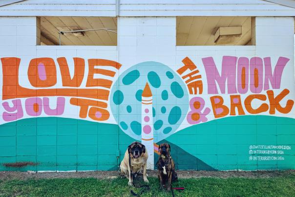 Two dogs in front of a colorful mural that reads "love you to the moon in back" in South Huntsville.