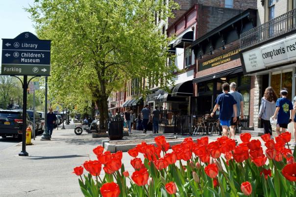 People walking along Broadway sidewalk with red tulips