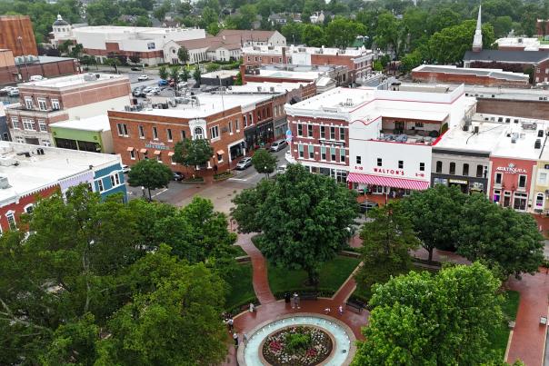 Bird's eye view of the Bentonville square, featuring a circular fountain surrounded by lush trees, and the city's historic main street in the background.