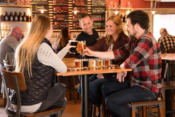A group of friends cheers while sitting at a table in a brewery.