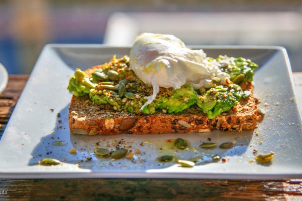 a white ceramic plate with a piece of seeded toast covered in smashed avocado and a poached egg