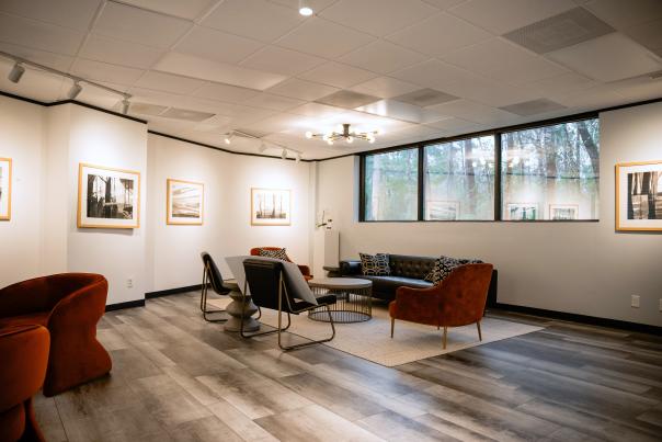 Inside The Woodlands Arts Council gallery. It looks like a large office or a small reception room with black leather couches, burnt orange fabric chairs, and a small art exhibition on the walls. This collection consists of abstract, black and white ink paintings of trees.