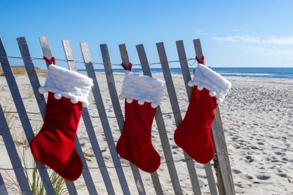 3 red Christmas stockings hanging from sand fence on the beach