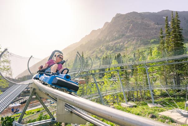 Woman looking like she is going fast around a corner on a single person coaster with sky and mountains around her