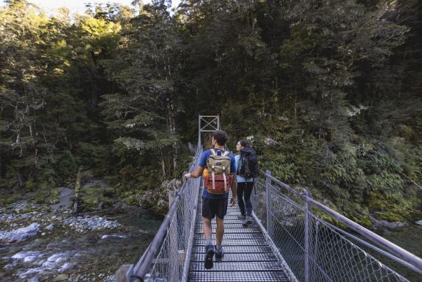 People crossing bridge into native bush at the start of the Routeburn Track