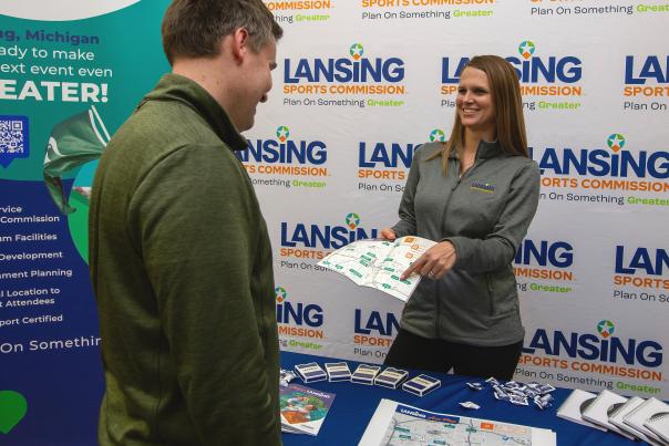 A Lansing Sports Commission staff member shares visitor information at a welcome booth.