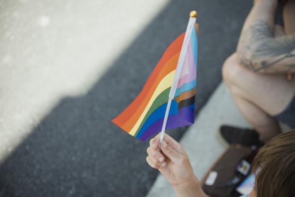Peron holding a small progressive pride flag as it flaps in the wind