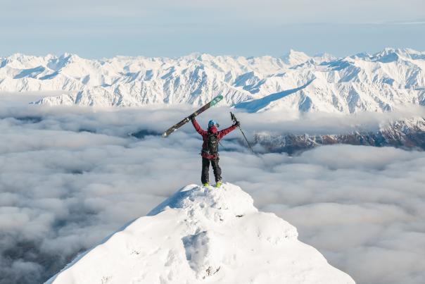 Person standing on the summit of a mountain with snowy peaks in the distance